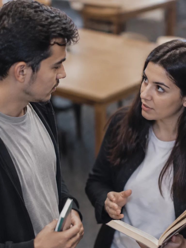 Duas participantes conversando de pé no corredor entre prateleiras de livros